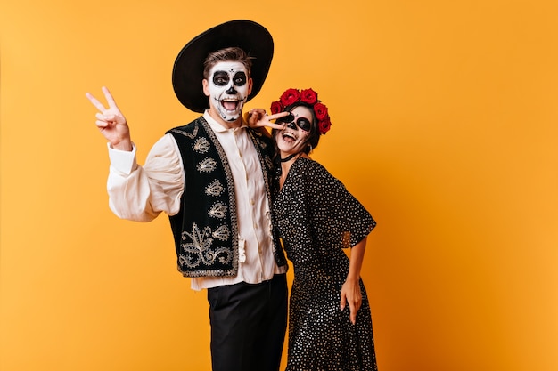 Free photo emotional dark-haired boy and his girlfriend are having fun in mexican clothes showing peace sign.