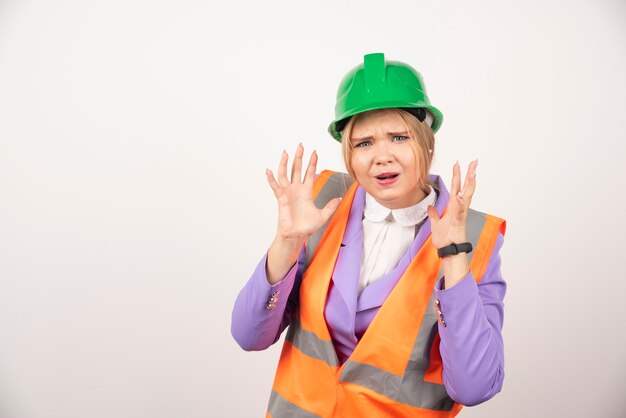 Emotional female builder in helmet on white wall. 