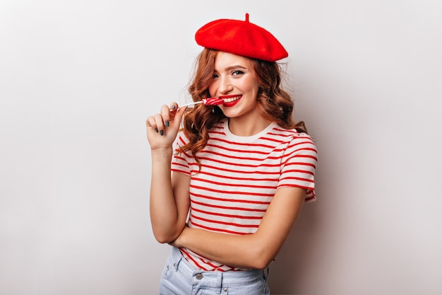 Free photo emotional french girl in t-shirt eating lollipop. enchanting curly woman enjoying candy.