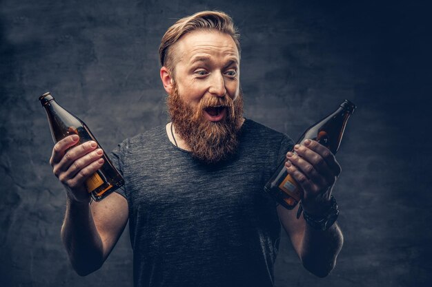 Emotional, funny redhead bearded drunk hipster male holds craft bottled beer.