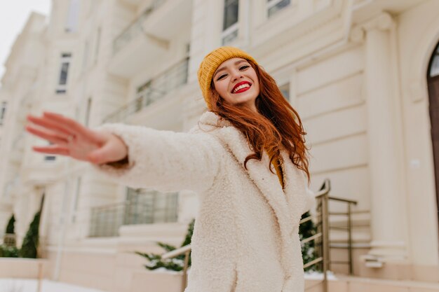 Emotional ginger girl in winter outfit posing with smile. Outdoor portrait of adorable red-haired woman with happy face expression.