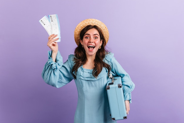 Emotional girl excitedly shows tickets for plane and retro luggage. Woman rejoices on upcoming journey.