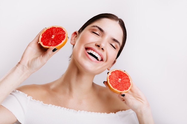 エネルギーに満ちた感情的な女の子は、赤い柑橘系の果物を手に笑ってポーズをとります。