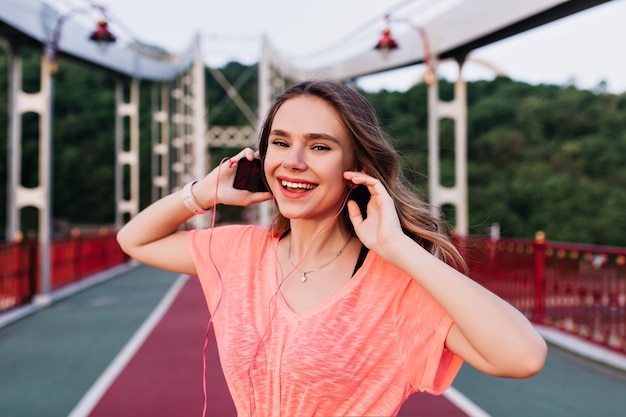 Emotional girl in pink t-shirt enjoying favorite song after training. Adorable caucasian woman preparing for marathon.