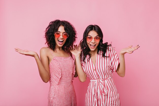 Emotional girls make surprised face expression. Lady in summer pink sunglasses posing for portrait.