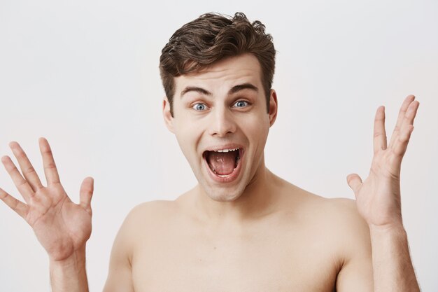 Emotional glad smiling with open mouth man has appealing appearance, trendy hairstyle, rejoice success. Young european muscular man holding palms open, being surprised and happy.