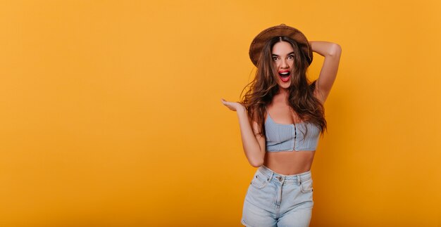 Emotional gorgeous woman in stylish tank-top touching her elegant hat