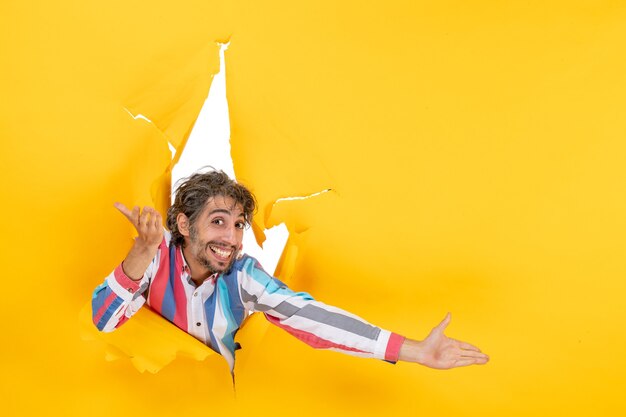 Emotional happy and smiling young man in torn yellow paper hole background