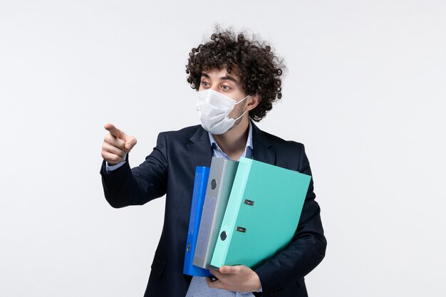 Emotional male entrepreneur in suit and wearing his mask holding documents pointing forward on white surface