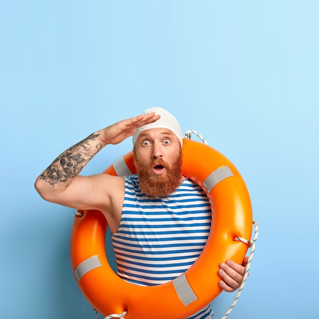 感情的な男性のライフガードが遠くを見つめ、海に沈んでいる人に気づき、人々が生き残るのを助けます