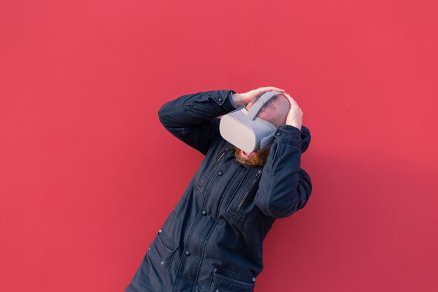 Emotional portrait of a man on the street wearing reality glasses against the background of a red wall