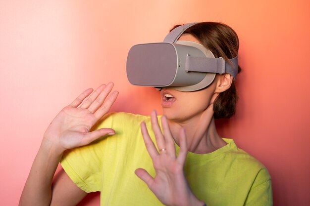 Emotional portrait of woman in virtual reality glasses in studio on pink orange background