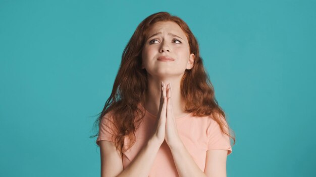 Эмоциональная рыжая девушка показывает жест на камеру на красочном фоне Молитвенное выражение