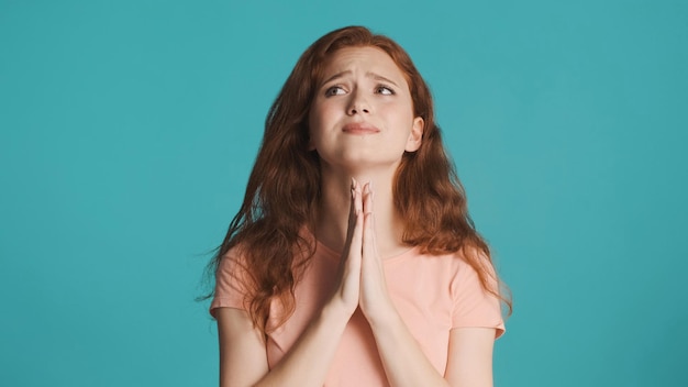 Emotional redhead girl showing please gesture on camera over colorful background Praying expression