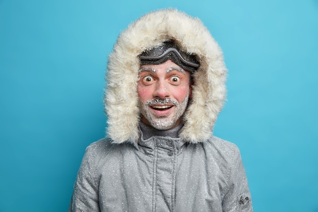 Emotional shocked cheerful man wears winter jacket has red face covered with ice cannot believe in astounding news.