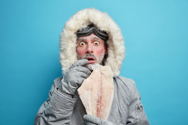 無料写真 冬のアウターを着た感情的なショックを受けた冷ややかな男は、北の場所の低温時に凍った魚を非常に冷たく感じます。