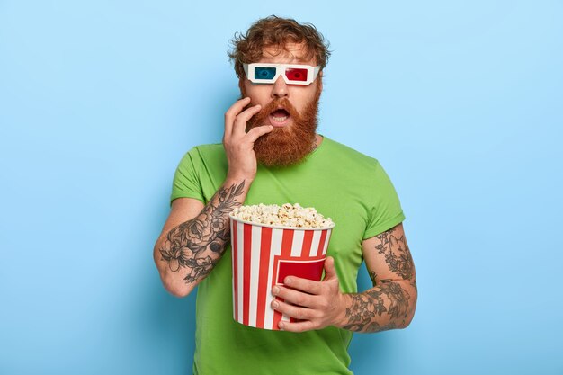 Emotional stupefied red haired man stares at camera through cinema glasses