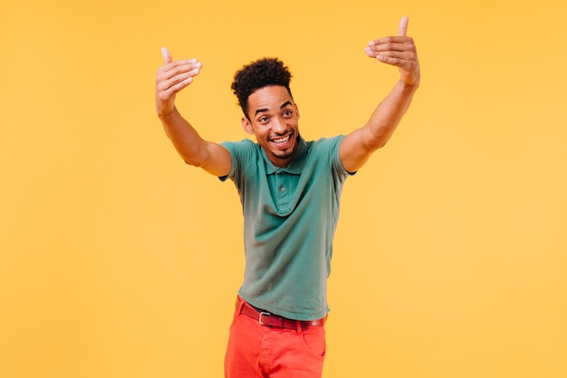 Emotional stylish man in green t-shirt having fun. Carefree black guy waving hands.