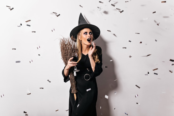 Free Photo emotional witch in black hat drinking blood. glad female wizard holding goblet with potion.