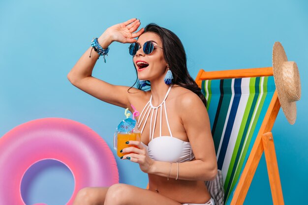 Emotional woman in bikini holding glass of juice and looking away