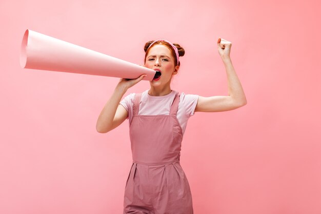 Emotional woman with appeal shouts into mouthpiece on pink background.