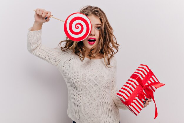 Donna emotiva con bel trucco e bella manicure, chiude un occhio con enormi caramelle al caramello