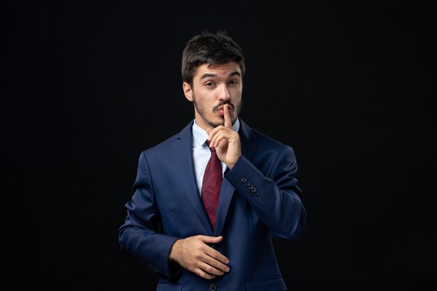 Emotional and young bearded man making silence gesture on isolated dark wall