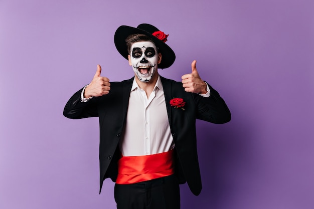 Free photo emotional young guy in classic suit and red satin belt joyfully raised his thumbs up.