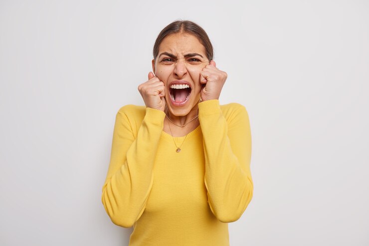 Free Photo emotional young woman exclaims loudly keeps mouth wide opened yells wears casual yellow jumper has unhappy stressful expression isolated over grey wall