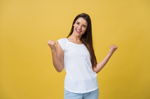 Emotions, expressions, success and people concept - happy young woman or teenage girl celebrating victory isolated over yellow background.