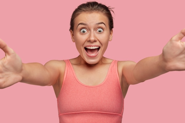 Бесплатное фото Эмоциональная спортивная женщина позирует у розовой стены