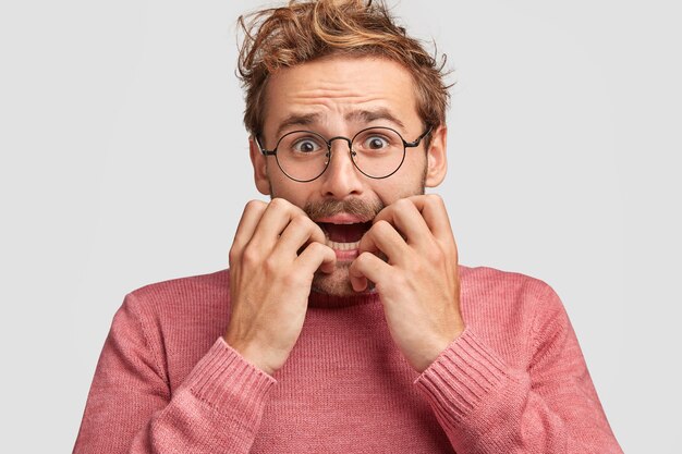 Emotive depressed young embarrassed man bites fingernails in panic, looks with nervous expression