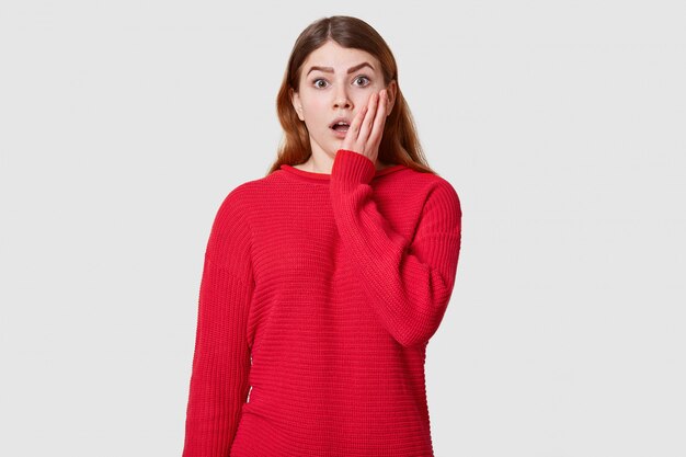 Emotive portrait of beautiful fashionable girl dressed red sweater posing over white