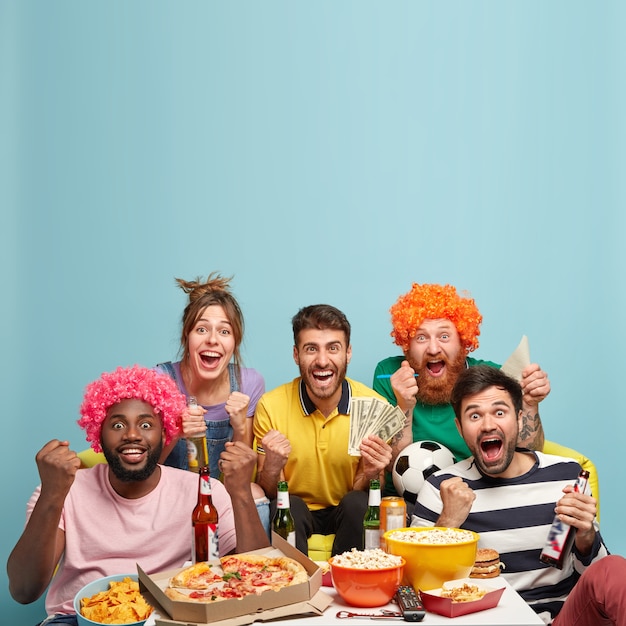 Free photo emotive screaming men and woman support favourite football team, cheer up, hold dollar banknotes and soccer ball, make winning gesture