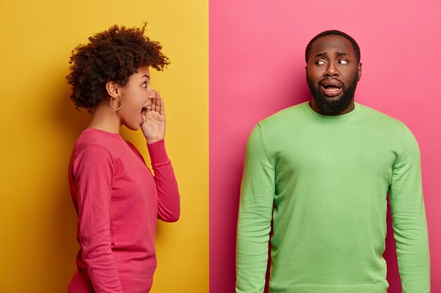 Emotive young curly woman stands in profile and screams loudly at guilty man