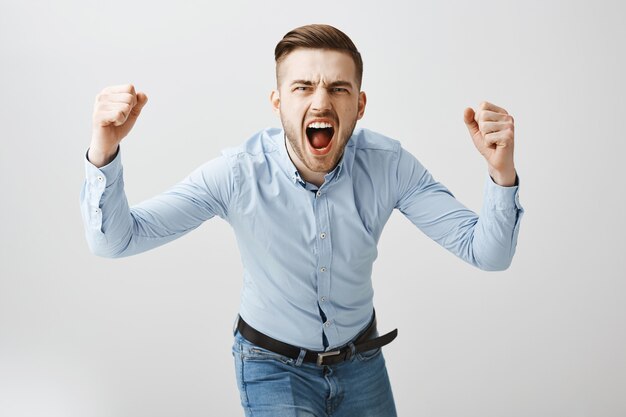 Emotive young man clench fists and screaming aggressive, watching sport game