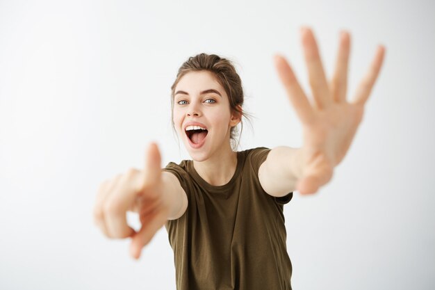 Emotive young woman looking stretching hands to camera with opened mouth.