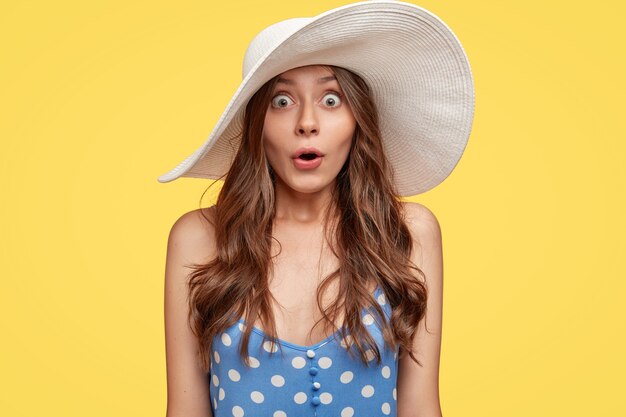 Emotive young woman wearing a hat posing against the yellow wall