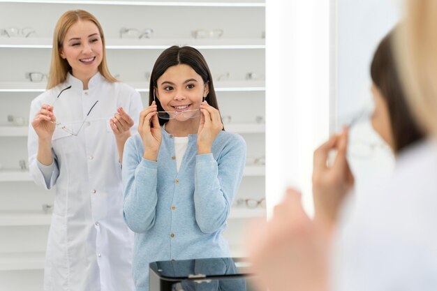 Employee helping girl to try on glasses