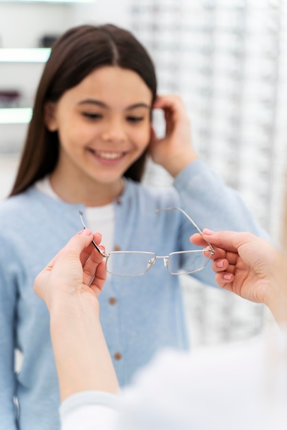 Employee helping girl to try on glasses
