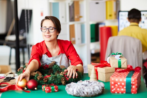 Foto gratuita dipendente che fa una ghirlanda di natale e confeziona scatole regalo