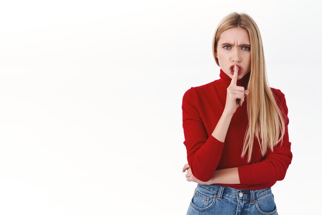 Employee management and confident women concept Angry serious blond female shushing shhh with finger over lips frowning mad tell be quiet need silence standing white background
