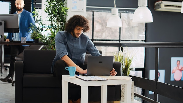 Foto gratuita il dipendente esamina le statistiche sul laptop mentre lavora alla strategia di sviluppo online, sviluppatore ai. analista professionista che esamina rapporti di informazioni di marketing, spazio aperto aziendale unicorno.