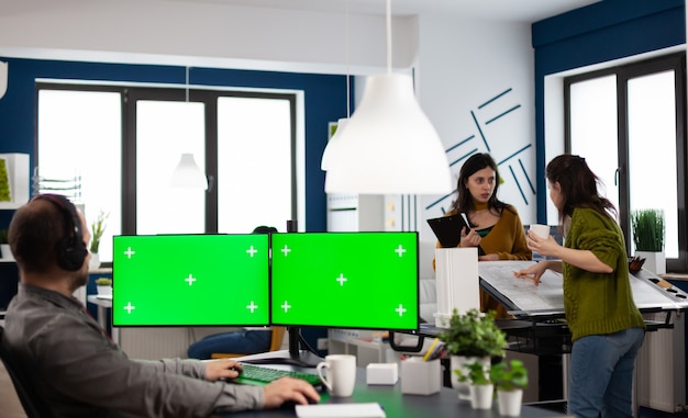 Сотрудник с наушниками, использующий настройку двойного монитора с зеленым экраном, макет цветного ключа на изолированном дисплее, сидя в студии видеопроизводства