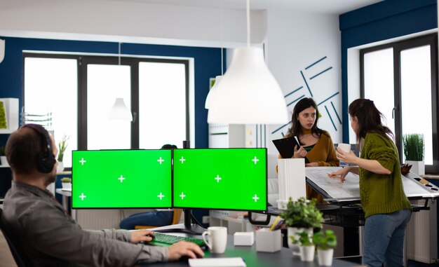 Employee with headphones using dual monitror setup with green screen, chroma key mock up isolated display sitting in video production studio