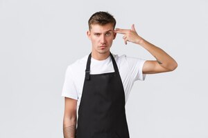 Employees, grocery stores and coffee shop concept. bothered and distressed barista making fake gun sign over head and grimacing pissed-off, shooting himself tired, white background