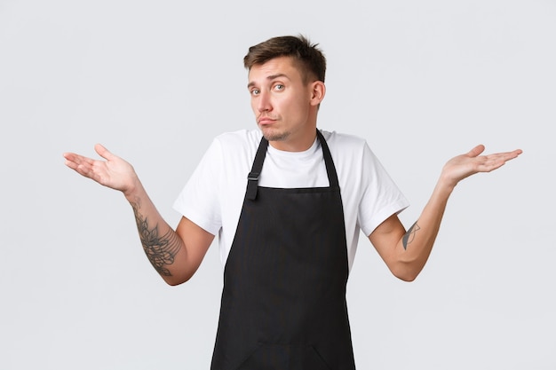 Employees, grocery stores and coffee shop concept. Clueless and indecisive handsome barista shaking head unaware and shrugging, dont know what say, have no idea, white background