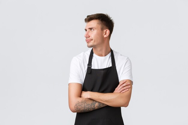 Employees, grocery stores and coffee shop concept. Displeased grumpy barista, cafe worker in black apron feeling mad or offended, turn away sulking and cross arms chest, white background