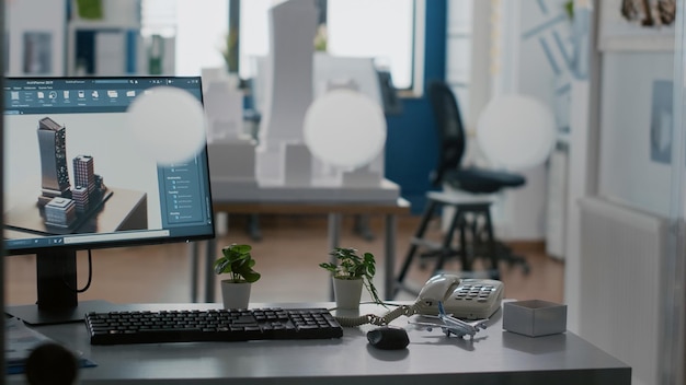 Empty architectural workplace with building model and 3d construction layout on table. Nobody in office with computer and tools used for urban development and architecture design.