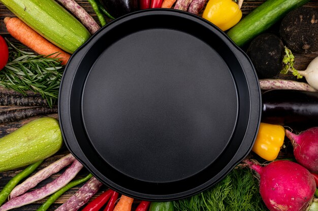 Пустая черная сковорода со свежими овощами вокруг